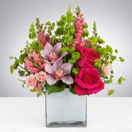 Pink roses and orchids arranged in a clear square vase