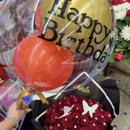Birthday balloon bouquet with gold and red balloons over red roses