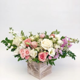 Low floral arrangement of pink, white, and lavender roses in a square vase