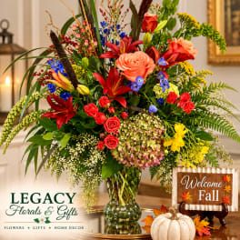 Colorful mixed bouquet in a glass vase with a fall welcome sign and pumpkin decor