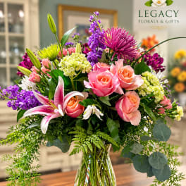 Colorful mixed bouquet in a clear glass vase with roses, lilies, and purple blooms
