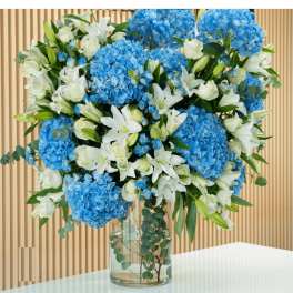Blue hydrangeas and white lilies in a clear glass vase