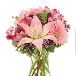 Pink lilies, gerbera daisies, and mixed blooms arranged in a clear glass vase