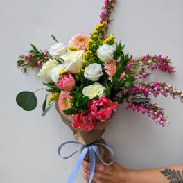 Hand-tied bouquet of white and pink flowers wrapped in brown paper with a blue ribbon