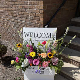 Colorful flower arrangement around a welcome sign for a baptism