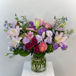 Mixed bouquet of pink, purple, and white flowers in a clear glass vase