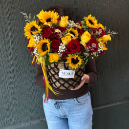 Large bouquet of red and yellow roses with sunflowers in a woven basket