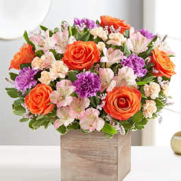 Mixed bouquet of orange roses, pink alstroemeria, and purple carnations in a wooden box