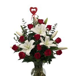 Red roses and white lilies in a clear glass vase with a heart pick