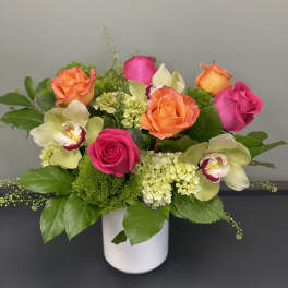 Pink and orange roses with orchids in a white vase
