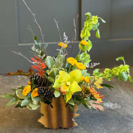 Autumn floral arrangement with yellow orchid, mums, pinecones, and fall leaves in a rustic container