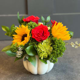 Red roses and yellow sunflowers in a white pumpkin vase