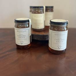 Group of jars of burnt caramel sauce on a wooden surface with one raised on a wood stand
