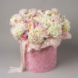 Pink and white flower arrangement in a round pink box with ribbon