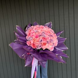 Large bouquet of pink and lavender roses wrapped in purple paper