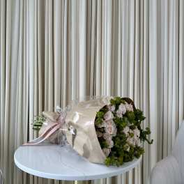 Bouquet of pale pink roses wrapped in beige paper with a pink ribbon