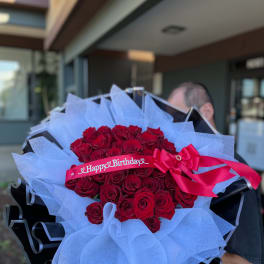 Bouquet of red roses wrapped in white paper with a pink birthday ribbon