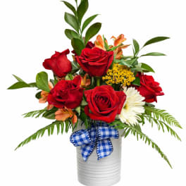 Red roses and mixed flowers in a white vase with a blue check ribbon