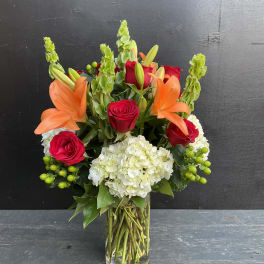 Bouquet of red roses, orange lilies, and white hydrangea in a glass vase