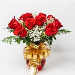 Red roses arranged in a vase with white filler flowers and a gold bow