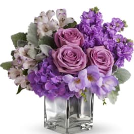 Purple roses and mixed lavender flowers in a clear glass vase
