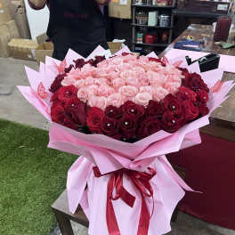Large bouquet of pink and red roses wrapped in pink paper with a ribbon