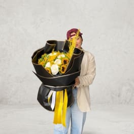 Person holding a large bouquet of white and yellow flowers wrapped in black paper