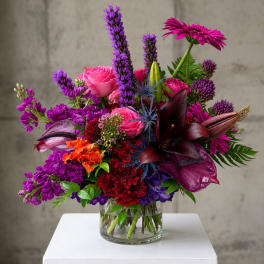 Mixed bouquet of pink, purple, and red flowers in a clear glass vase