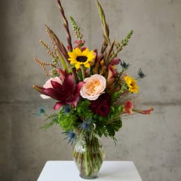 Mixed bouquet in a clear glass vase with sunflowers, roses, and lilies