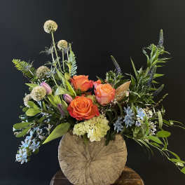 Mixed bouquet with orange roses, lilies, and blue flowers in a rustic vase