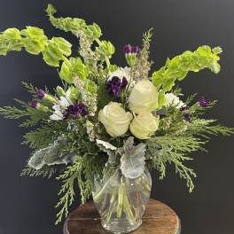 White roses and purple flowers in a clear glass vase with bright green foliage