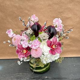 Pink and white floral arrangement with dark calla lilies in a green glass vase