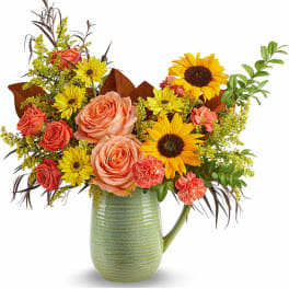 Mixed bouquet of roses, sunflowers, and daisies in a green ceramic pitcher