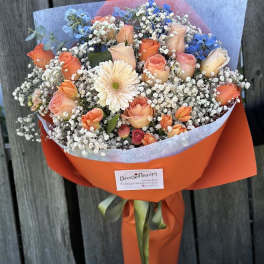 Bouquet of peach roses, blue flowers, and white baby's breath wrapped in orange paper