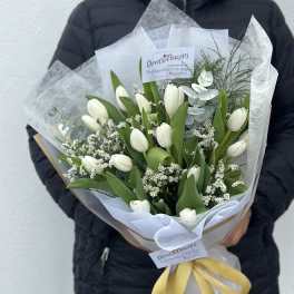White tulips arranged in a wrapped bouquet with a yellow ribbon