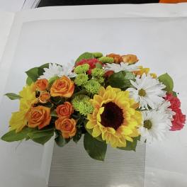Mixed bouquet with sunflowers, orange roses, white daisies, and pink carnations in a box