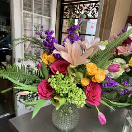 Mixed bouquet with pink roses, lilies, and purple flowers in a glass vase