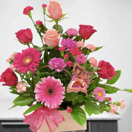 Pink and peach roses, gerbera daisies, and carnations in a pink box with a butterfly accent