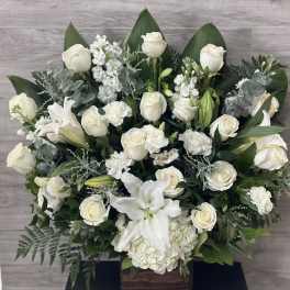 White roses and lilies arranged in a wooden box with greenery.