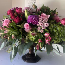 Large pink and purple floral arrangement in a dark pedestal vase