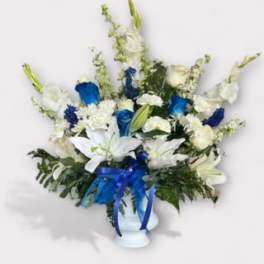 White and blue floral arrangement in a white vase with a blue ribbon