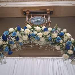 Large floral arch of blue and white roses beneath a wall clock