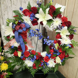 Circular wreath of red, white, and blue flowers on a black stand