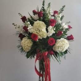 Tall bouquet of red roses and white hydrangeas in a glass vase with red ribbon