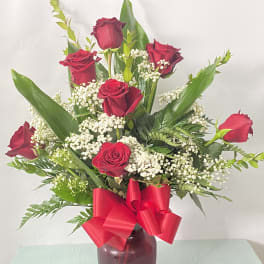 Red roses arranged in a vase with baby's breath and a red ribbon
