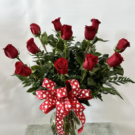 Red roses in a glass vase with a heart-patterned ribbon