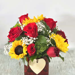 Bouquet of red roses and yellow sunflowers in a square vase with a heart tag