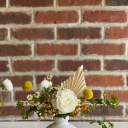 White floral arrangement in a white vase with yellow accents