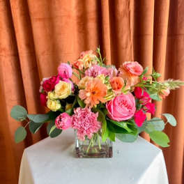 Mixed pink and peach flower arrangement in a square glass vase