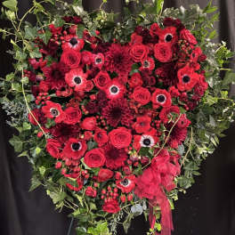 Heart-shaped red floral arrangement with ivy and a ribbon bow